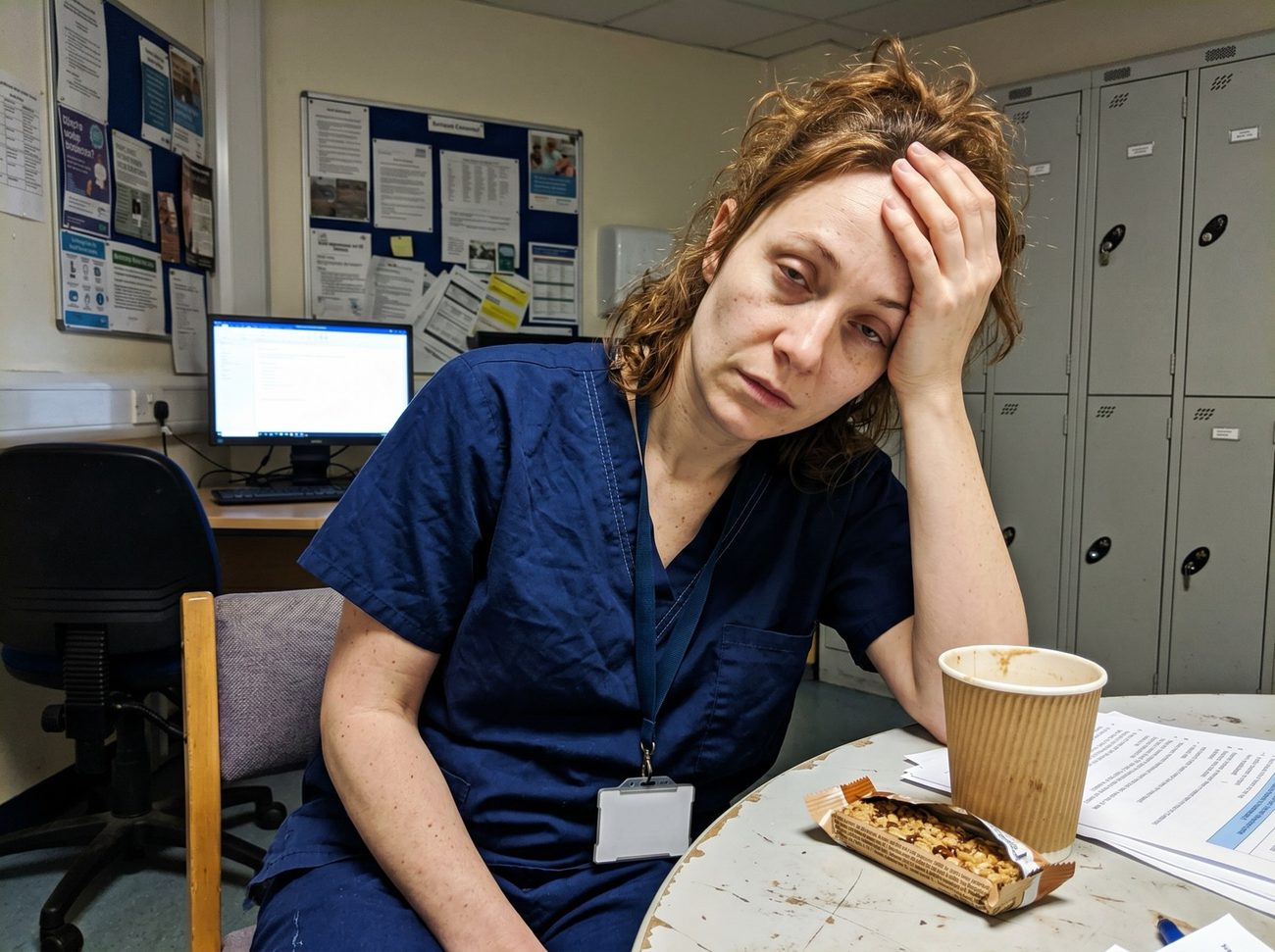 Exhausted nurse slumped in a hospital break room at 4 AM, head in her hand, running on empty