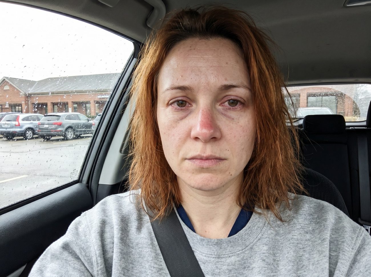 Exhausted nurse sitting in her parked car after a night shift, eyes red from crying, staring blankly ahead