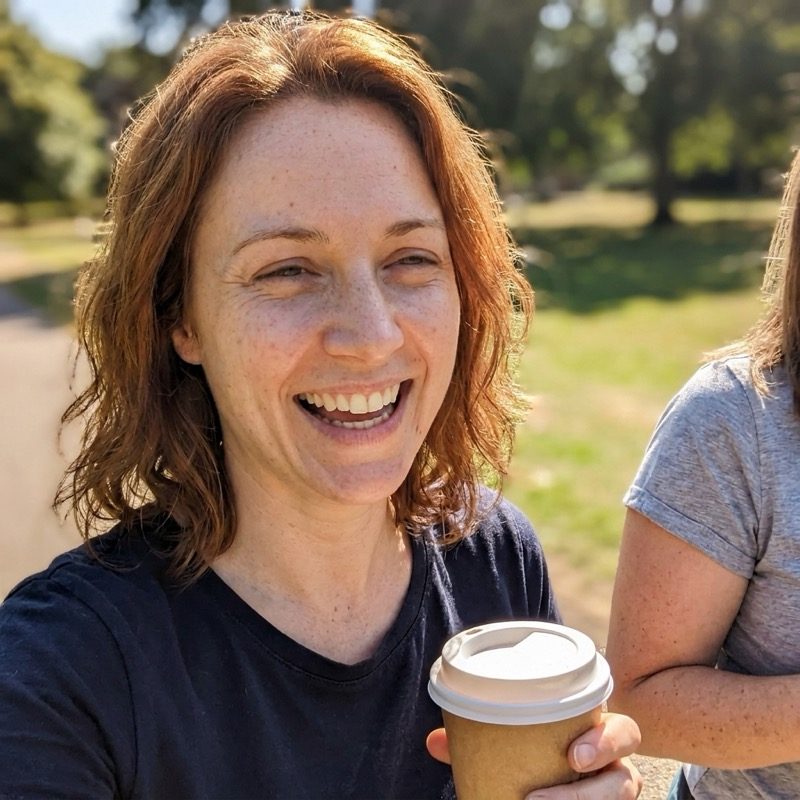 Rachel laughing outdoors with a coffee on a sunny day